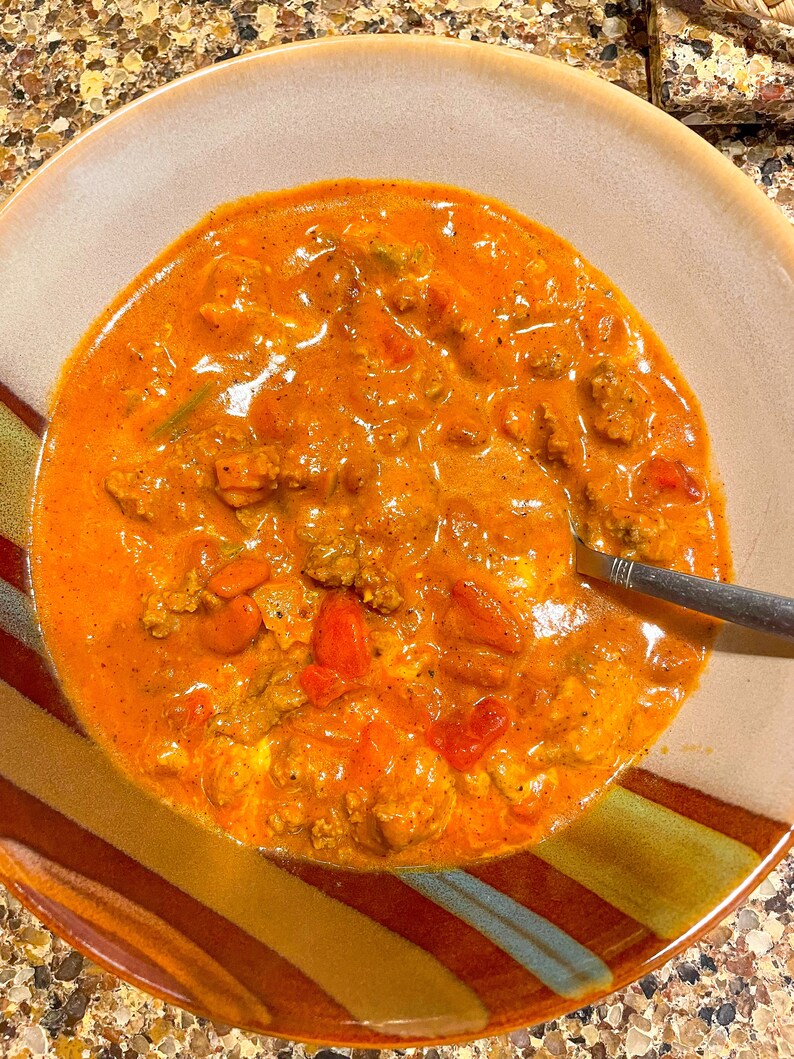 Peut inclure: Un bol de chili avec du b&oelig;uf hach&eacute;, des haricots et des tomates. Le chili est d'une couleur rouge fonc&eacute; et est surmont&eacute; d'une cuiller&eacute;e de cr&egrave;me fra&icirc;che.