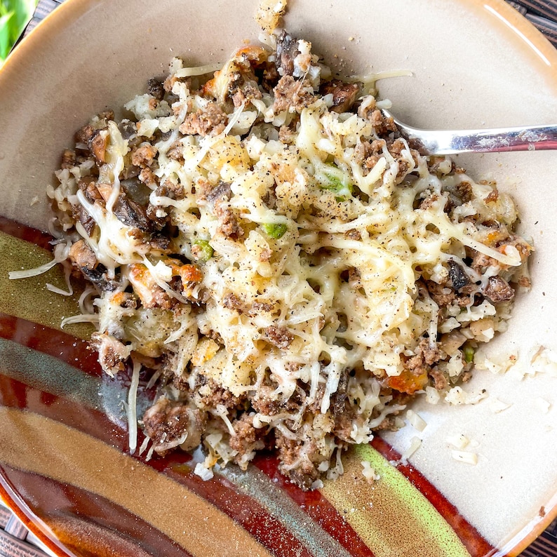 Peut inclure: Un gros plan d'un bol de b&oelig;uf hach&eacute; au fromage, de riz, de champignons et de petits pois. Le bol a un motif ray&eacute; brun et blanc.