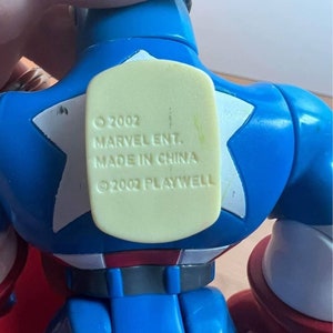 以下が含まれることがあります： キャプテンアメリカの青と赤のプラスチック製アクションフィギュア。フィギュアは、胸に白い星がついた青と赤の衣装を着ています。フィギュアは右手に赤い盾を持っています。フィギュアの背中には、「&copy; 2002 MARVEL ENT. MADE IN CHINA &copy; 2002 PLAYWELL」と書かれた黄色のステッカーが付いています。