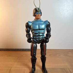 May include: A blue and silver action figure with a black helmet and antennas. The figure is wearing black boots and has red accents on the legs.