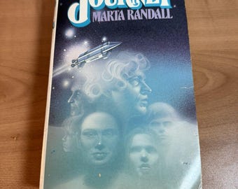 May include: A paperback book cover with a blue and black background. The title "Journey" is in large white letters. The author's name, "Maria Randall", is in smaller white letters below the title. The cover features a spaceship flying through space and a group of people's faces.