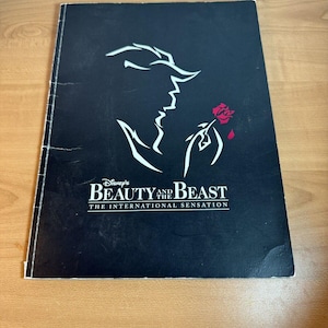 Könnte beinhalten: Schwarzweißes Programmcover für Disneys Die Schöne und das Biest, die internationale Sensation. Das Cover zeigt eine Silhouette des Biestes, das eine rote Rose hält.
