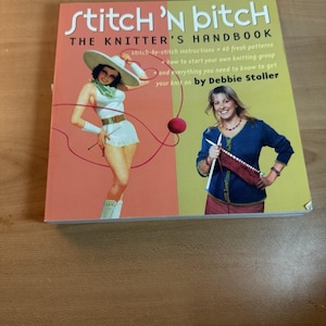 Puede incluir: El libro "Stitch 'N Bitch: The Knitter's Handbook" de Debbie Stoller. La portada presenta un diseño dividido con una ilustración vintage de una mujer con un atuendo de vaquera a la izquierda y una mujer tejiendo a la derecha. El libro incluye instrucciones y patrones de tejido.