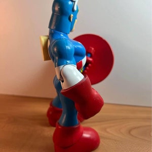 以下が含まれることがあります： 青いプラスチック製のキャプテンアメリカのフィギュア。フィギュアは右手に赤い盾を持っています。フィギュアは胸に白い星、頭に白いストライプがあります。