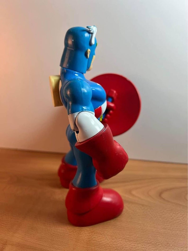 以下が含まれることがあります： 青いプラスチック製のキャプテンアメリカのフィギュア。フィギュアは右手に赤い盾を持っています。フィギュアは胸に白い星、頭に白いストライプがあります。