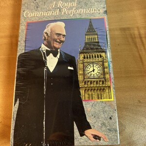Puede incluir: Una cinta VHS con Red Skelton en una actuación titulada "A Royal Command Performance". La portada presenta una foto de Red Skelton con un esmoquin, sonriendo y sosteniendo un micrófono. El fondo es una foto del Big Ben en Londres.