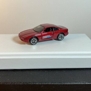 May include: A red toy car model of a BMW 8 series with the text "BMW M-Tech" on the side.