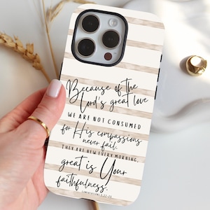 May include: A white and beige striped phone case with a black border. The case features the text "Because of the Lord's great love...great is Your faithfulness." The case is held by a hand with a gold ring.