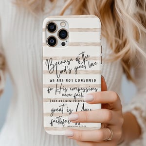 May include: A white phone case with horizontal beige stripes and black script. The script reads "Because of the Lord's great love... His compassions never fail... great is His faithfulness." The case is held in a hand.