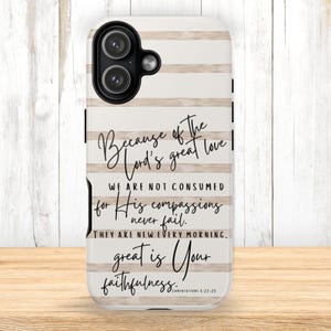 May include: A white and beige striped phone case with the text "Because of the Lord's great love...great is Your faithfulness." The case has a black camera cutout and is on a wooden surface.
