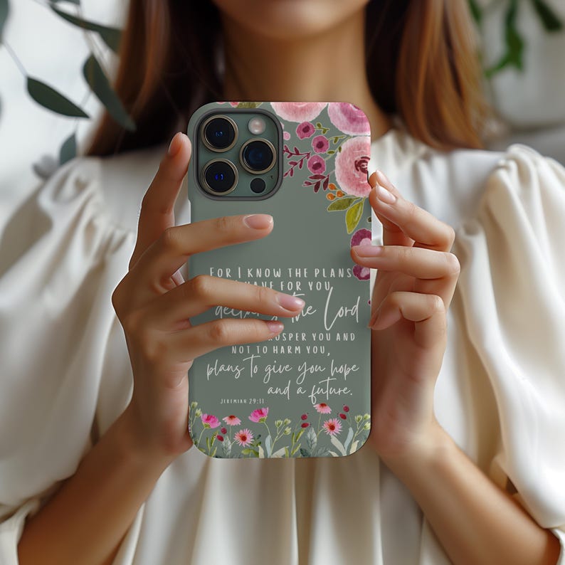 May include: A sage green phone case with a floral design and text. The case features pink and purple flowers in the upper right corner and along the bottom. The text reads "For I know the plans I have for you...plans to give you hope and a future."