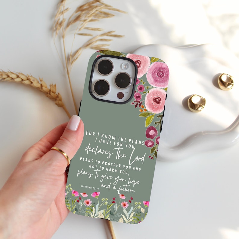 May include: Sage green phone case with a floral design featuring pink and purple flowers. The case has a black border and includes the text "For I know the plans I have for you, declares the Lord, plans to prosper you and not to harm you, plans to give you hope and a future."