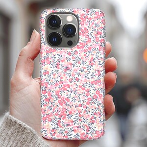 Pode incluir: Uma capa de telefone branca com um padr&atilde;o floral rosa e branco. A capa tem um recorte para a lente da c&acirc;mera.