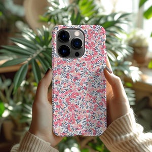 Pode incluir: Uma capa de telefone branca com um padr&atilde;o floral rosa e azul. A capa tem um recorte para a lente da c&acirc;mera na parte de tr&aacute;s.