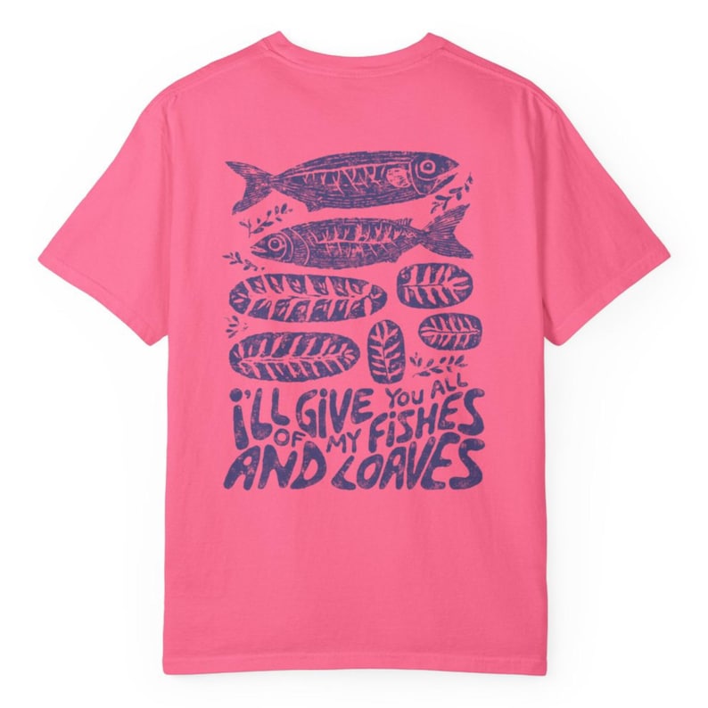 May include: A pink t-shirt with a purple graphic design on the back. The design includes two fish, several loaves of bread, and the text "I'll give you all of my fishes and loaves."