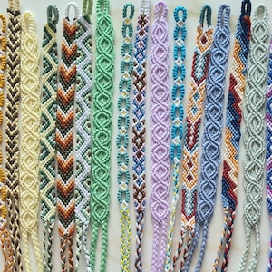 May include: A collection of 25 colourful friendship bracelets with various patterns and designs. The bracelets are made with colourful embroidery floss and are tied with knots.