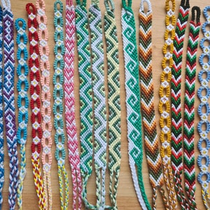 May include: A collection of colourful friendship bracelets with various patterns, including chevron, geometric, and floral designs. The bracelets are made with colourful embroidery floss and are tied with knots.