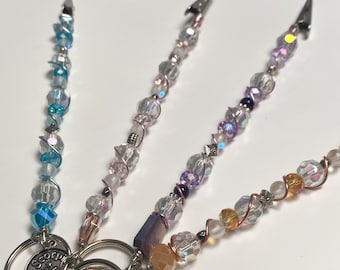 May include: Three beaded keychains with different colored beads and charms. The first keychain has blue and white beads with a silver charm that says "Scorpio". The second keychain has pink and white beads with a silver star charm. The third keychain has orange and white beads with a silver owl charm.