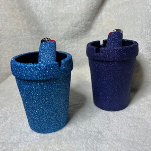 May include: Two glitter ashtrays, one blue and one dark blue, with a lighter in each.
