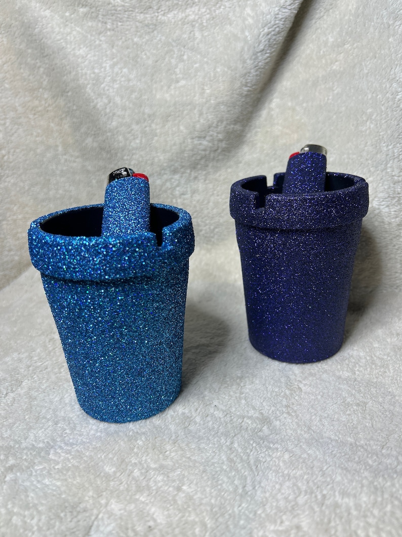 May include: Two glitter ashtrays, one blue and one dark blue, with a lighter in each.