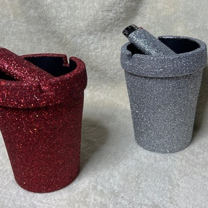 May include: Two glitter-covered ceramic ashtrays, one red and one silver, with a lighter in each.