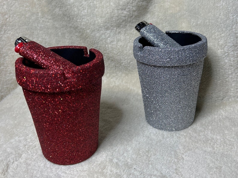 May include: Two glitter-covered ceramic ashtrays, one red and one silver, with a lighter in each.