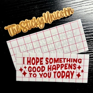May include: A wooden sign with the text "The Sticky Unicorn" in a cursive font. Below are two white vinyl decals with red text that reads "I HOPE SOMETHING GOOD HAPPENS TO YOU TODAY" with star accents.