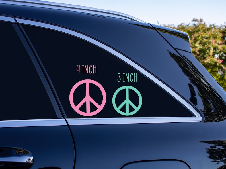 May include: Two peace sign decals on a black car window. The larger decal is 4 inches and pink. The smaller decal is 3 inches and green.
