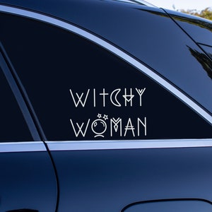 May include: A black car with a white vinyl decal on the back window that reads "Witchy Woman" with a stylized moon and stars graphic.
