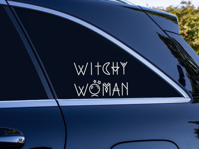 May include: A black car with a white vinyl decal on the back window that reads "Witchy Woman" with a stylized moon and stars graphic.