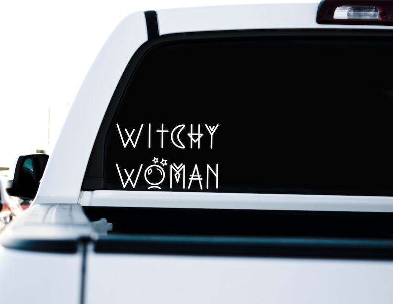May include: A white truck with a black rear window. The window has a white vinyl decal that reads "Witchy Woman" with a crescent moon and a crystal ball graphic.