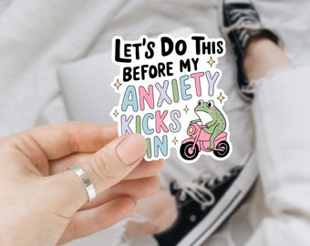 May include: A sticker with a frog riding a motorcycle and the text "Let's do this before my anxiety kicks in". The text is in rainbow colors and the frog is green.