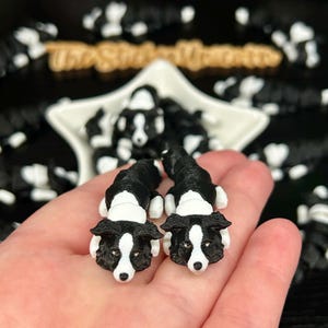 May include: Two small, articulated figurines shaped like black and white Border Collie dogs. Each figurine features a detailed head with pointed ears, a white blaze on the face, and a segmented body structure that allows for movement and flexibility.