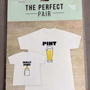 May include: A package of two iron-on transfers featuring white t-shirt designs. The larger shirt graphic says PINT with a beer glass illustration, and the smaller shirt graphic says HALF PINT with a baby bottle illustration. Text reads THE PERFECT PAIR.