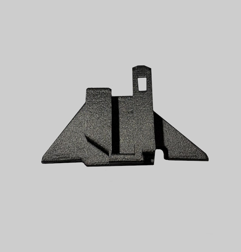 Puede incluir: Un objeto geom&eacute;trico gris oscuro con una superficie texturizada. Presenta una torre rectangular con una abertura cuadrada, una base triangular y un soporte vertical central. El dise&ntilde;o es sim&eacute;trico y parece ser de metal.