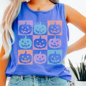 Pode incluir: Uma regata azul sem mangas com uma grade de nove ab&oacute;boras de Halloween coloridas. Cada ab&oacute;bora est&aacute; em um quadrado diferente, com cores como laranja, roxo e verde-azulado. A parte de cima &eacute; combinada com jeans azul claro.