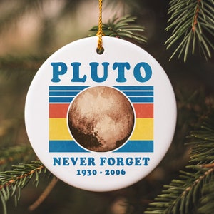 May include: A white ceramic Christmas ornament with a blue and yellow retro design featuring the planet Pluto and the text "PLUTO NEVER FORGET 1930-2006".