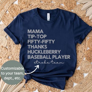 May include: A navy blue short-sleeve t-shirt featuring grey text that reads MAMA, TIP-TOP, FIFTY-FIFTY, THANKS, HUCKLEBERRY, BASEBALL PLAYER, and stroke team in a script font. The shirt has a crew neckline and a standard fit.