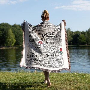 May include: A white throw blanket with black text and a red rose design. The text includes words like "romance", "mafia", "gothic", "kinky", "spicy", and "paranormal".