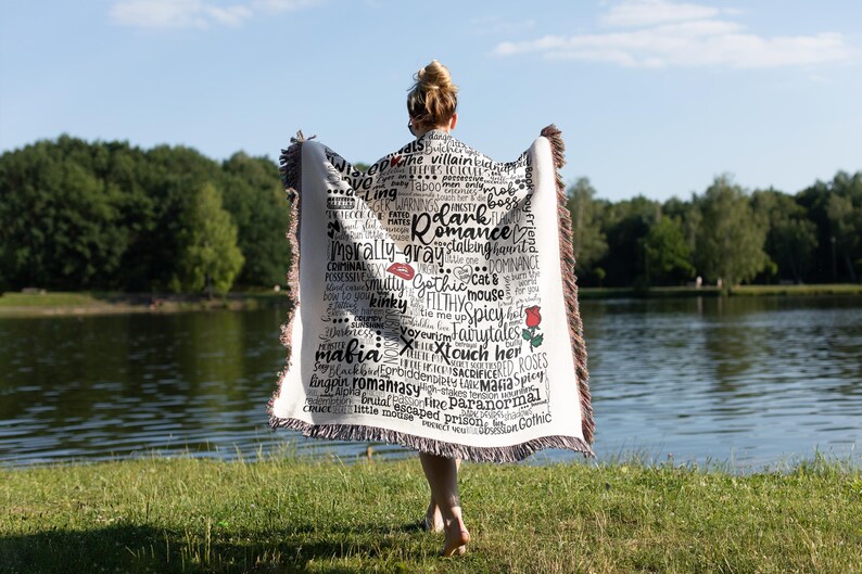 May include: A white throw blanket with black text and a red rose design. The text includes words like "romance", "mafia", "gothic", "kinky", "spicy", and "paranormal".