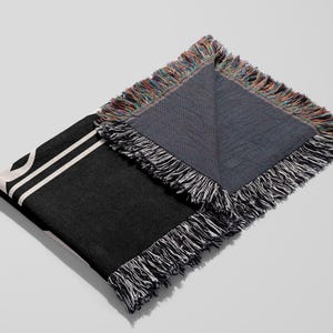 Puede incluir: Manta de tejido negro y blanco con borde de flecos. La manta est&aacute; doblada por la mitad, mostrando el lado trasero, que es de un color azul oscuro s&oacute;lido.