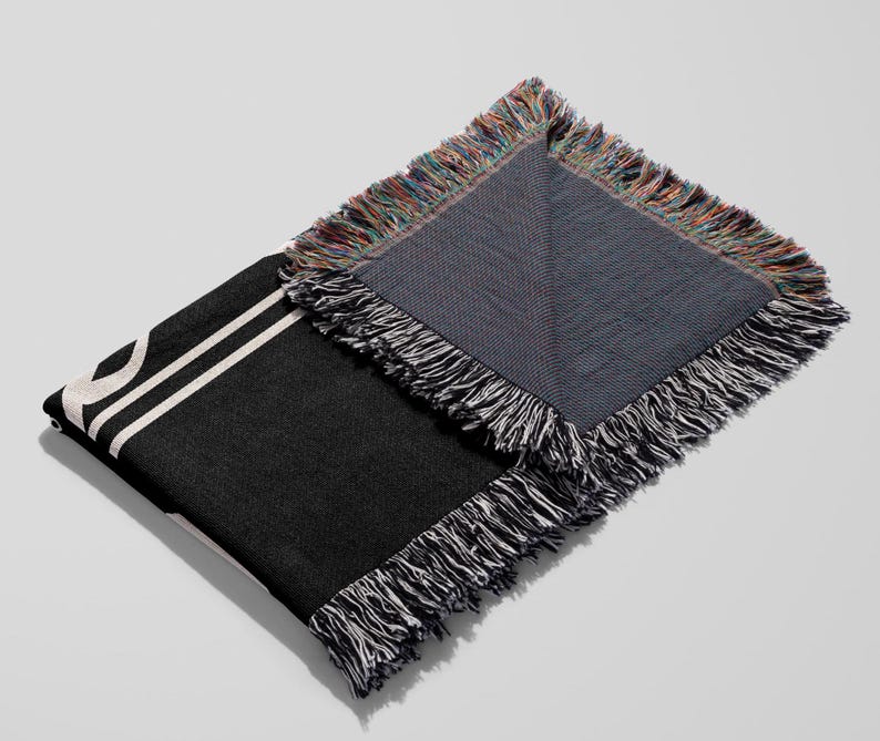 Puede incluir: Manta de tejido negro y blanco con borde de flecos. La manta est&aacute; doblada por la mitad, mostrando el lado trasero, que es de un color azul oscuro s&oacute;lido.
