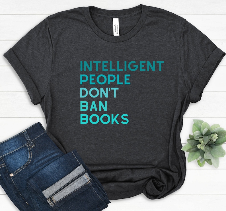 May include: A dark heather grey t-shirt with the text "INTELLIGENT PEOPLE DON'T BAN BOOKS" in teal blue lettering.
