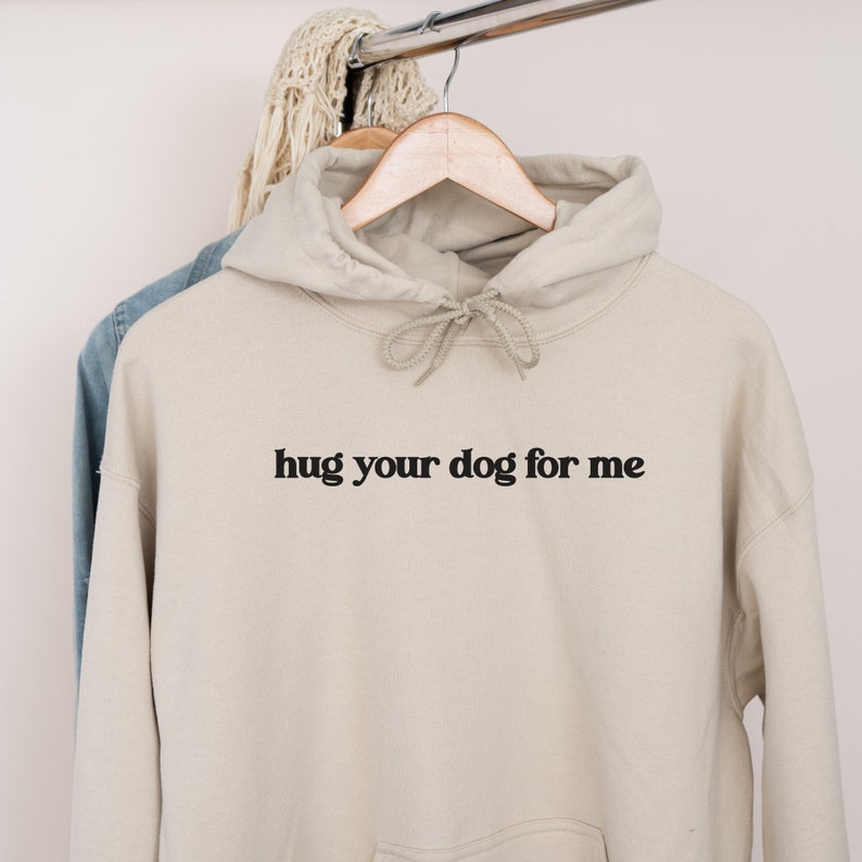 Pu&ograve; includere: Una felpa con cappuccio beige con una stampa nera che dice "hug your dog for me".