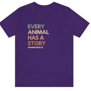 May include: A purple t-shirt with the text "EVERY ANIMAL HAS A STORY" in green, tan, and orange. The hashtag "#ANIMALRESCUE" is below the text. The shirt is made of a soft material.