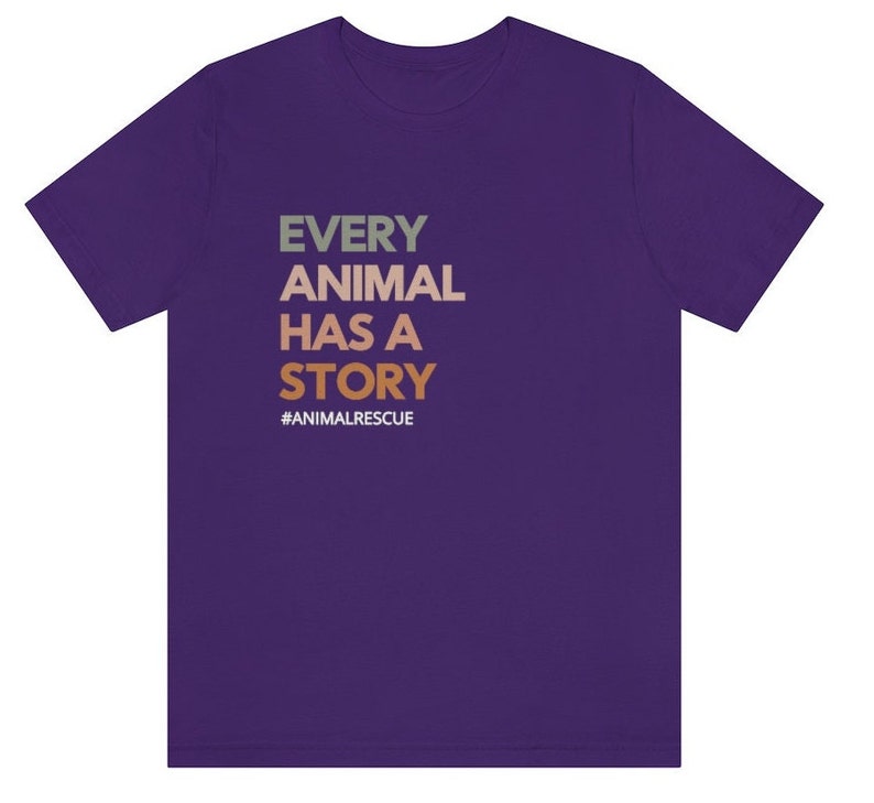 May include: A purple t-shirt with the text "EVERY ANIMAL HAS A STORY" in green, tan, and orange. The hashtag "#ANIMALRESCUE" is below the text. The shirt is made of a soft material.