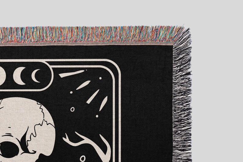 Puede incluir: Manta de tejido negro y blanco con un dise&ntilde;o de calavera y luna. La manta tiene un borde de flecos.