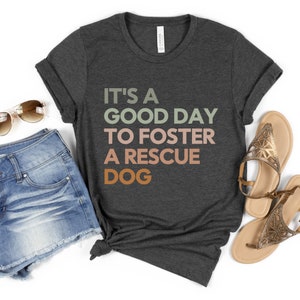 May include: A dark grey t-shirt with the text "It's a good day to foster a rescue dog" in a gradient of green, pink, and orange.
