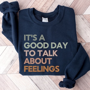 May include: A navy blue sweatshirt with the text "It's a good day to talk about feelings" printed in green, orange, and brown.