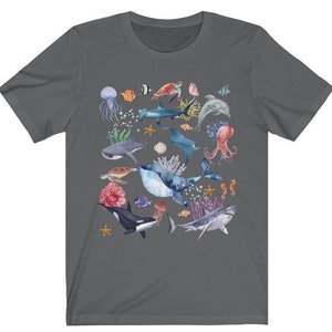 May include: A dark gray t-shirt with a colorful watercolor design of various sea creatures, including a whale, a shark, a manta ray, a jellyfish, a sea turtle, and a starfish.